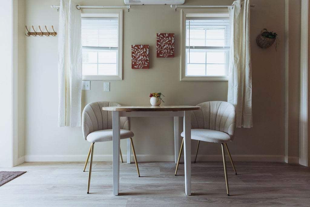 A dining area with a table and two chairs, a vase with flowers, and two wall-mounted artworks.