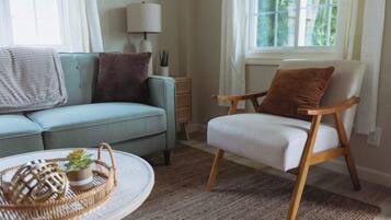 A living room with a light blue sofa, a wooden chair, a round coffee table, and a wicker tray with a plant.