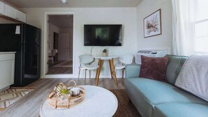 Een moderne woonkamer met een ronde salontafel, een bank, een televisie en een eethoek met stoelen.