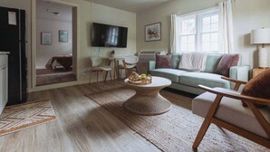 Een woonkamer met een bank, fauteuils, een salontafel, een flatscreen televisie en een raam met gordijnen.