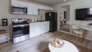 Een moderne keuken met witte kastjes, een magnetron, een fornuis en een koelkast. Er is een eethoek met een ronde tafel en stoelen.