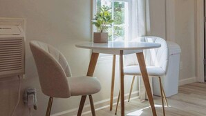 Une pièce avec une table ronde, deux chaises, une plante en pot et une fenêtre avec des rideaux.