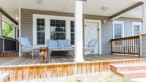 Une véranda couverte avec deux fauteuils en osier et un petit chien.