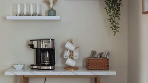 Un área de cocina con cafetera, tazas y una planta en un estante.