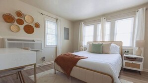 Un dormitorio con cama, mesitas de noche, escritorio y aire acondicionado de pared.