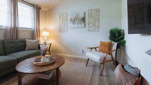 Una sala de estar con sofá, sillón, mesa de centro y obras de arte en la pared.