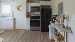 Een moderne keuken met witte kasten, een magnetron, oven en koelkast. Er is een eethoekje met een tafel en stoelen.