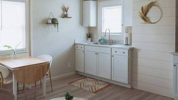 Eine moderne Küche mit weißen Schränken, einem Holztisch und einem Fenster mit Jalousien.