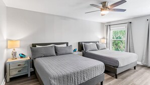 Habitació d'hotel amb dos llits, un ventilador de sostre, una tauleta de nit amb làmpada i una finestra amb cortines.