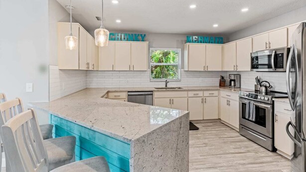 A modern kitchen with white cabinets, a granite island, stainless steel appliances, and pendant lighting. - Golf Cart, 2 bed 2 Bath, Heated Pool (Indian Rocks Beach)