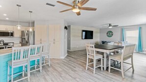 A modern kitchen with stainless steel appliances, a dining area with a wooden table and chairs, and a ceiling fan. - Golf Cart, 2 bed 2 Bath, Heated Pool (Indian Rocks Beach)