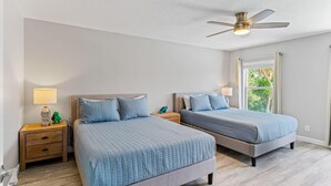 A bedroom with two beds, a ceiling fan, bedside tables with lamps, and a window with a view of trees. - Golf Cart, 2 bed 2 Bath, Heated Pool (Indian Rocks Beach)
