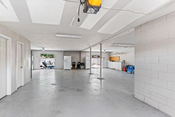 A spacious indoor area with concrete floors and white walls, featuring a ceiling-mounted light fixture and a visible door on the left. - Golf Cart, 2 bed 2 Bath, Heated Pool (Indian Rocks Beach)