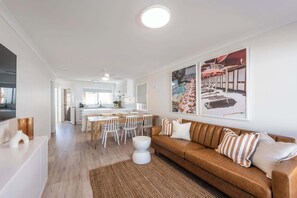 Ein modernes Wohnzimmer mit einer braunen Ledersofa, weißen Esstischen und einer Küche im Hintergrund.