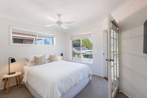 Une chambre à coucher avec un lit, deux fenêtres, un ventilateur de plafond et une porte.