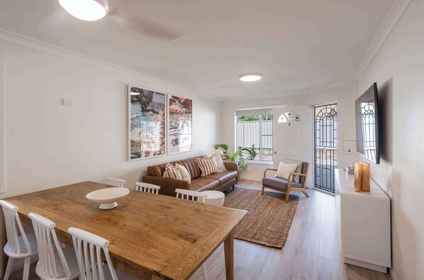 Un coin repas avec une table en bois et des chaises blanches, un canapé en cuir marron et un meuble blanc.