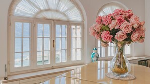 Une pièce avec une grande fenêtre, un vase rempli de roses roses et un vase bleu décoratif posé sur une table.