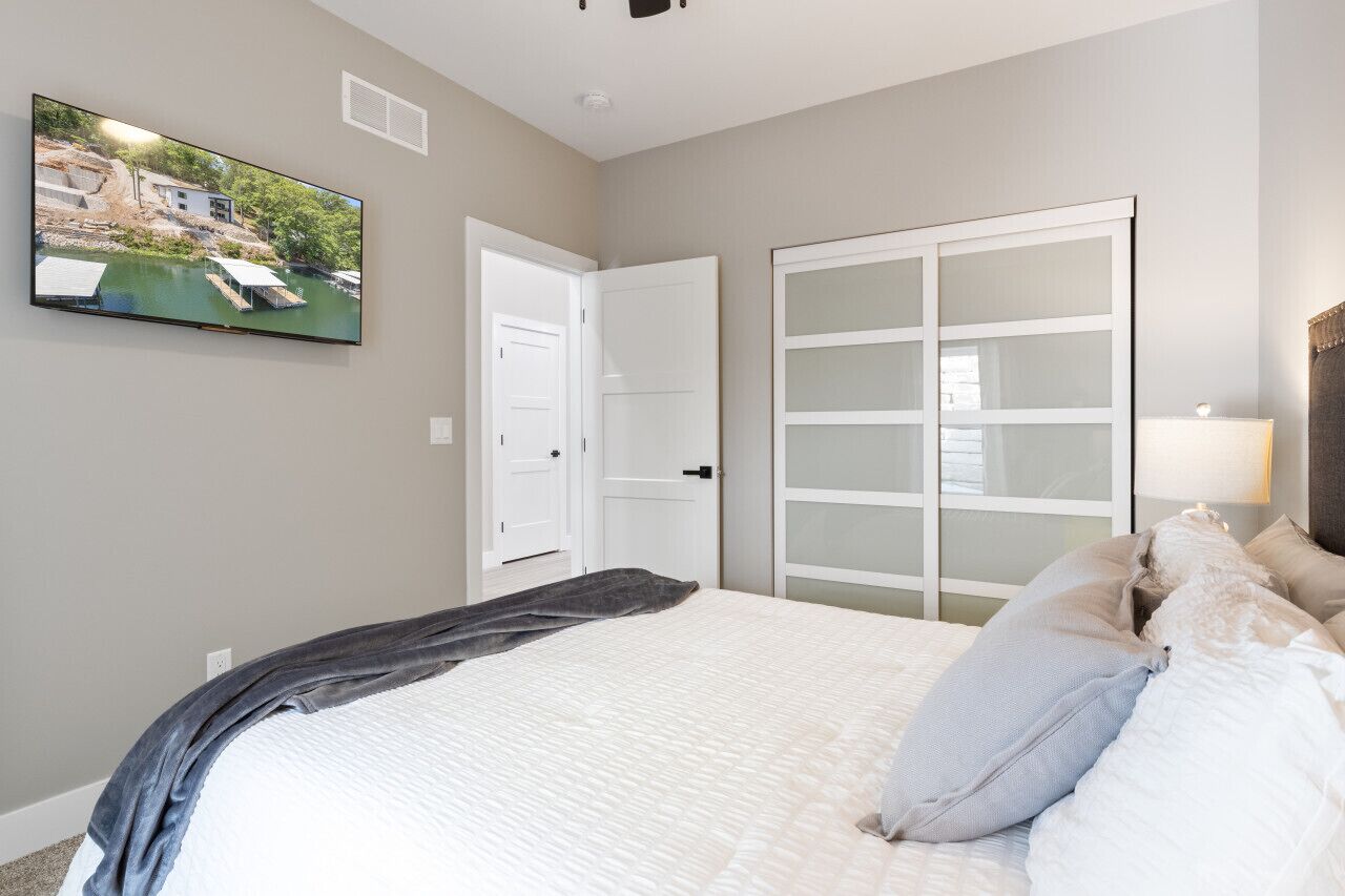 A bedroom with a bed, a flat-screen TV mounted on the wall, a wardrobe, and a sliding glass door.