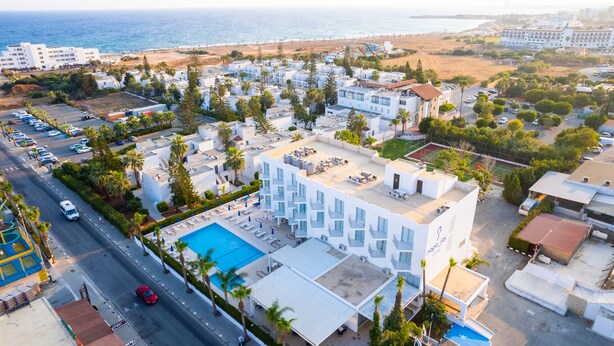An aerial view of a coastal hotel with a swimming pool, multiple balconies, and a beach view.
