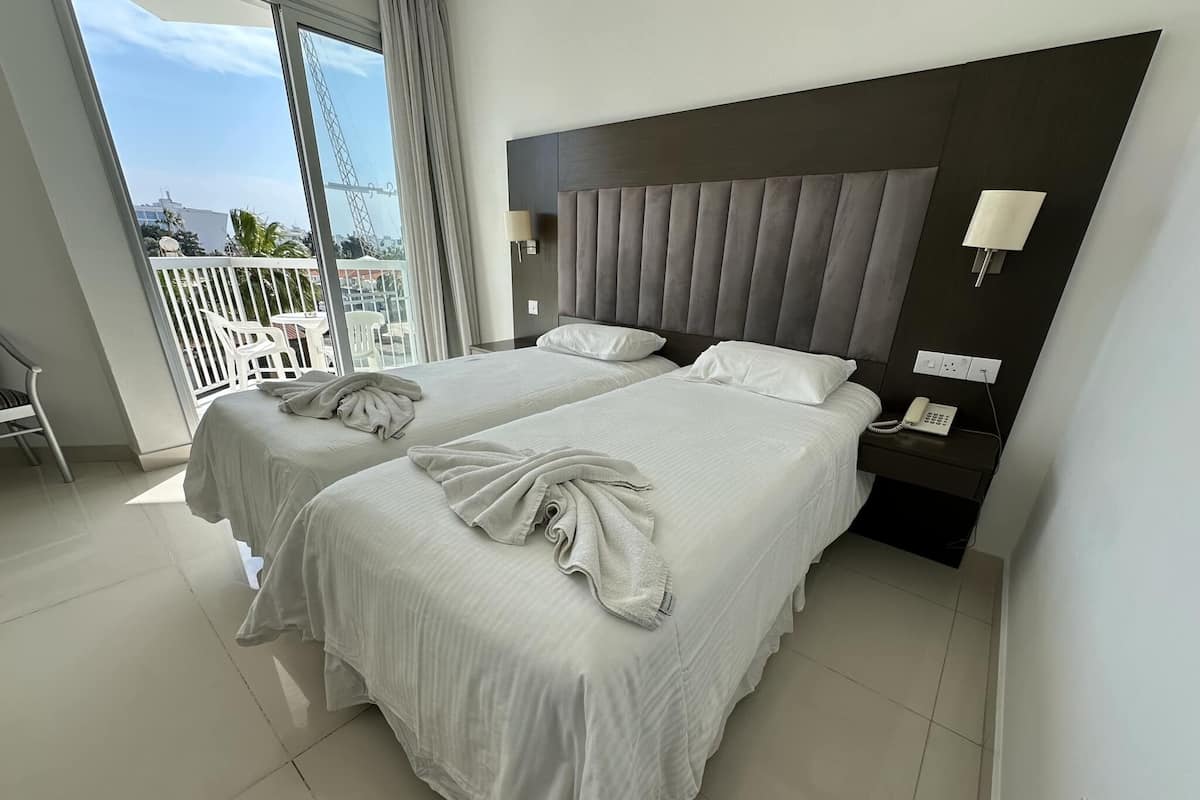 Habitación de hotel con dos camas, un balcón y un teléfono en la mesita de noche.