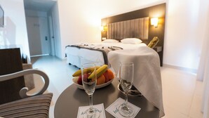 A hotel room with a bed, bedside table with fruit and glasses, and a chair.