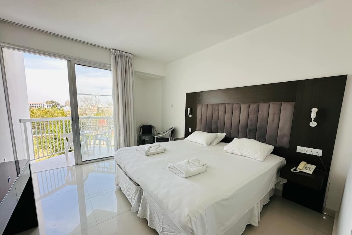 Habitación de hotel con una cama grande, teléfono en la mesita de noche y vista a la ciudad desde el balcón.