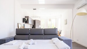 Quarto moderno com cama grande, cabeceira estofada cinza, roupa de cama branca e vista para o exterior.