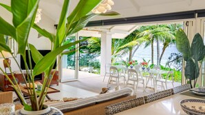 Una sala de estar moderna con un amplio ventanal que da a un jardín tropical y al mar.