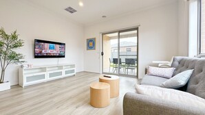 Un salon moderne doté d’un téléviseur à écran plat, d’un canapé gris, de petites tables d’appoint en bois et d’une porte-fenêtre coulissante donnant sur un patio extérieur.