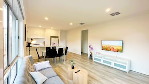Un salon moderne avec un canapé, une table basse et un téléviseur fixé au mur. Il y a également un coin cuisine avec des placards et un réfrigérateur.