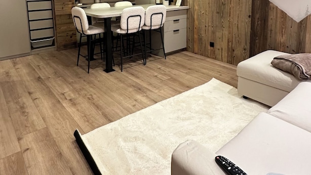 A modern kitchen with wooden ceiling and cabinets, a dining area with chairs, and a living area with a sofa and a remote control on it. - Appartement Samoëns (Samoëns)
