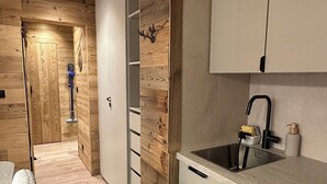 A modern kitchen with wooden accents, a built-in sink, and a hallway leading to a bathroom. - Appartement Samoëns (Samoëns)