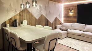 A dining area with a wooden ceiling, a long table with chairs, and a sofa in the background. - Appartement Samoëns (Samoëns)
