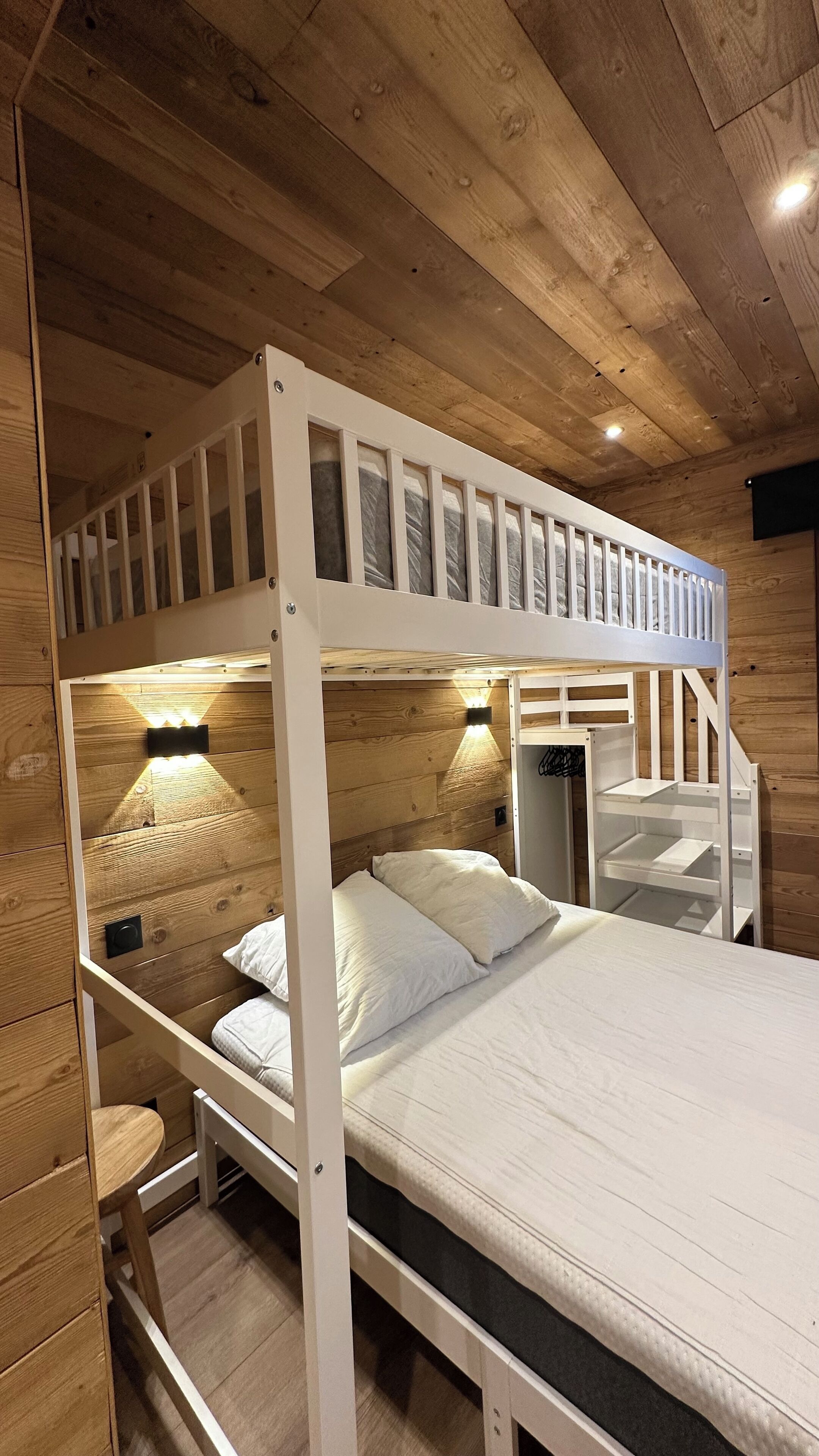 Uma cama de beliche com teto e paredes de madeira, um colchão branco e duas luminárias de cabeceira.