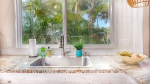 A kitchen with a large window, a sink, and a bowl of fruit on the counter. - Sunrise Tropical Garden Getaway (Pahoa)