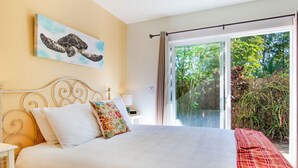 A bedroom with a large bed, a painting of a sea turtle, and a view of greenery through a sliding glass door. - Sunrise Tropical Garden Getaway (Pahoa)