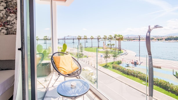 A balcony with a view of a waterfront promenade, a cactus plant, and a chair with a cushion. - Welcomely - Superior Room - Dith Piaf (Olbia)