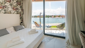 A hotel room with a bed, a view of the sea, and a balcony with chairs. - Welcomely - Superior Room - Dith Piaf (Olbia)