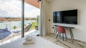 A hotel room with a large balcony, a bed with towels, a TV, and a chair. - Welcomely - Superior Room - Louis Armstrong (Olbia)
