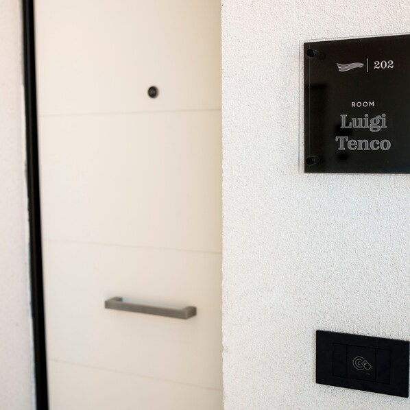A door with a handle and a wall-mounted sign indicating "ROOM 202 Luigi Tenco".