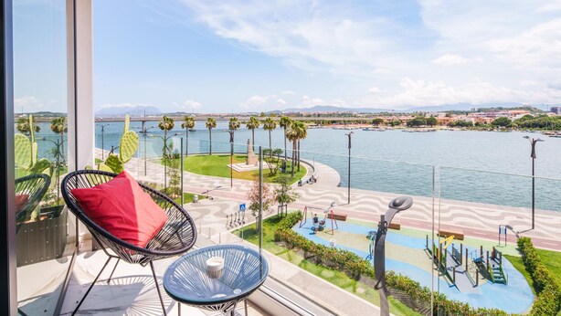Un balcón con vistas a un río, palmeras y un parque infantil.