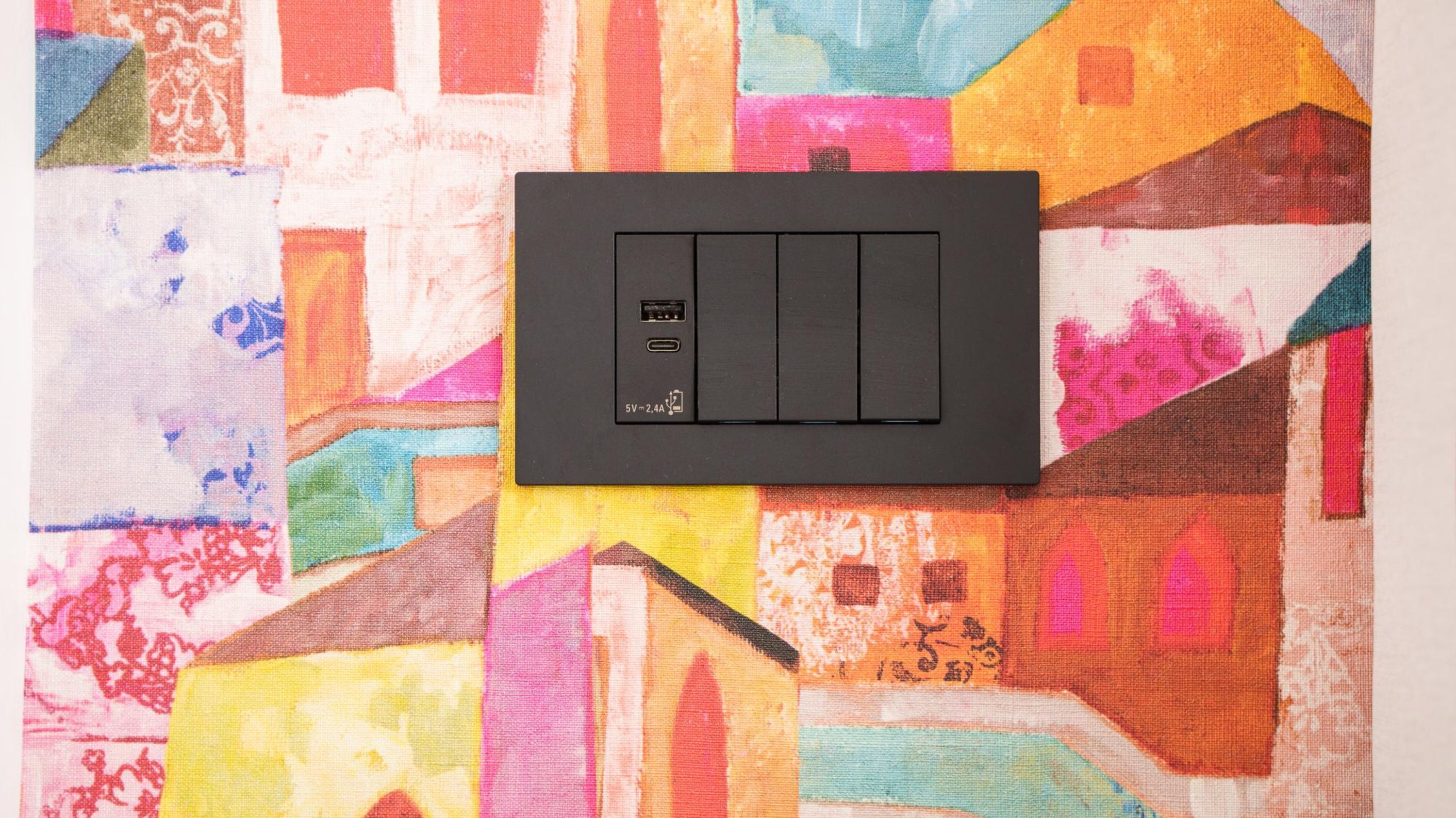 En svart grenuttag med två USB-portar och ett 5V 2,4A-uttag, placerad på en färgglad tygduk med geometriskt mönster.
