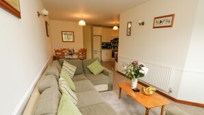 A living room with a sofa set, a coffee table with a vase, and a kitchen in the background. - Stags Cottage (South Molton)