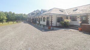 A row of white buildings with brick accents, a gravel driveway, and potted plants. - Stags Cottage (South Molton)