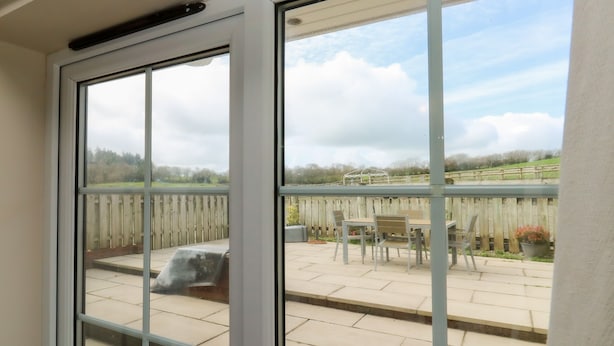 A view through a window to an outdoor patio with a wooden fence, a table, and chairs. - Stags Cottage (South Molton)