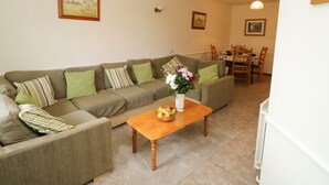 A living room with a sofa, a wooden coffee table with fruit, and a dining area in the background. - Stags Cottage (South Molton)