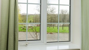 A window with a view of a grassy area and a wooden fence. - Stags Cottage (South Molton)