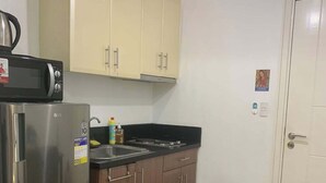 A compact kitchen with a refrigerator, microwave, and stove. There are cabinets, a sink, and a trash can. A dining table with chairs is visible. - 150 Newport condotel pasay  (Pasay)