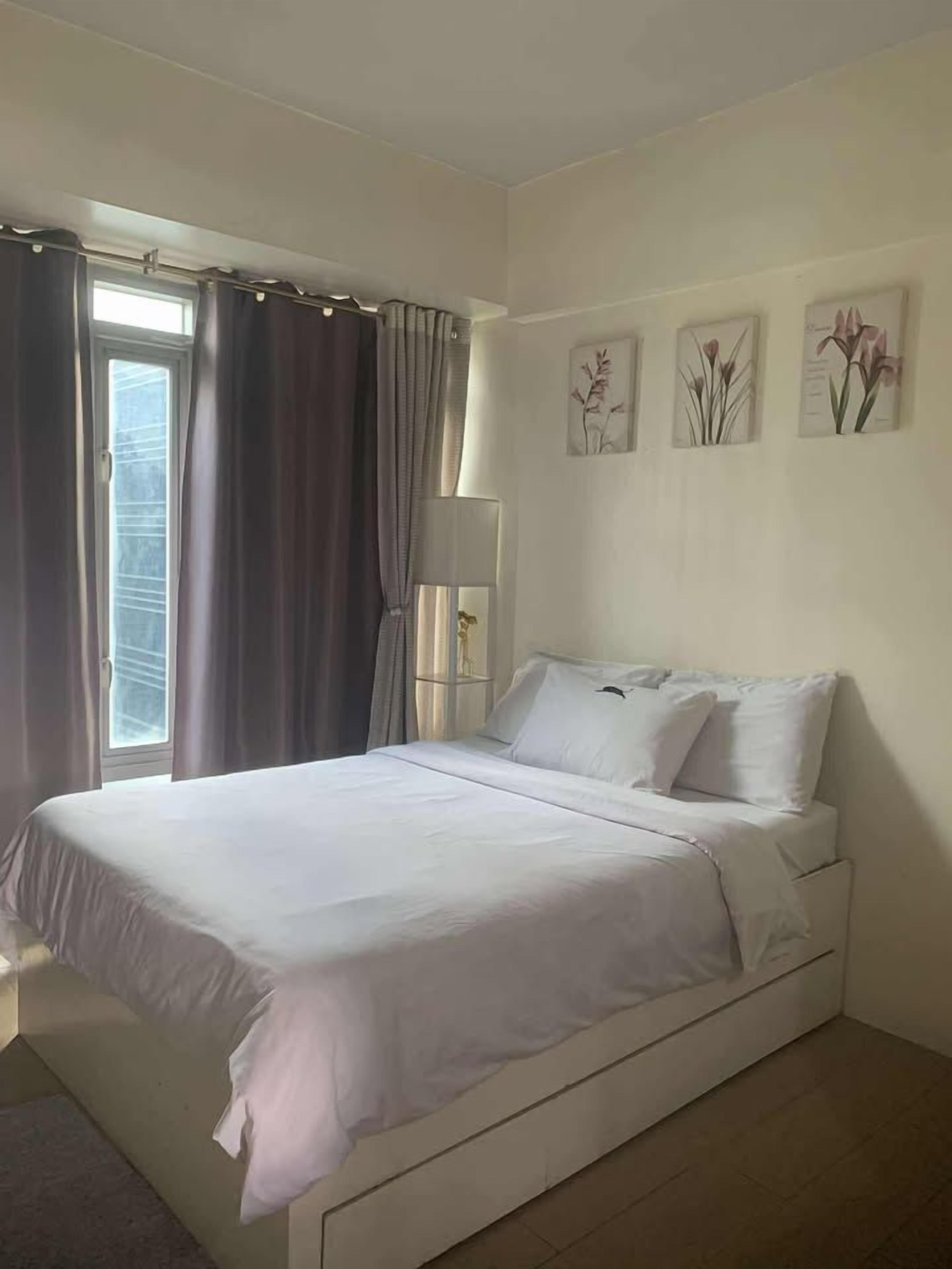 Un dormitorio con cama, cortinas, lámpara de noche y decoración en la pared.