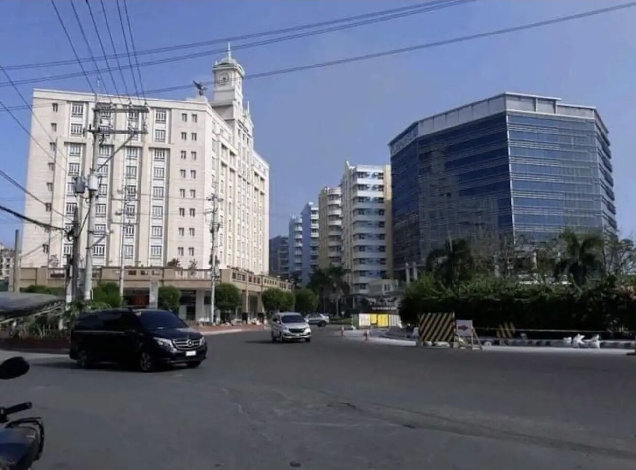 Una calle con edificios modernos, incluyendo un gran edificio blanco con una torre de reloj y un edificio de vidrio moderno.